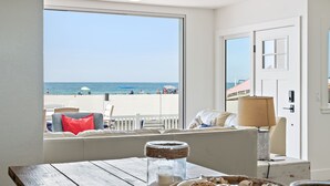 Ein Zimmer mit großem Fenster und Blick auf einen Strand, einem Holztisch mit Lampe und einem Bett mit Seeblick.