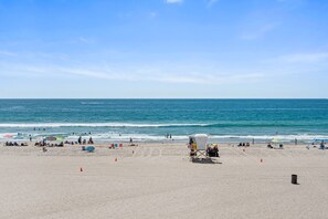 Une plage avec une tour de surveillance, des parasols et des personnes qui se prélassent au soleil.