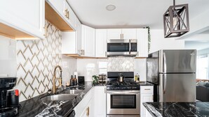 A modern kitchen with white cabinets, a black marble countertop, stainless steel appliances, and a geometric backsplash. - East Side Spa Retreat Near Lake, Restaurants and Fun (Milwaukee)
