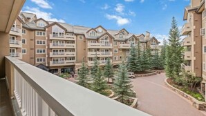 A multi-story residential building with balconies, a central courtyard with trees, and a clear sky. - Saint James Place 216 (Beaver Creek)