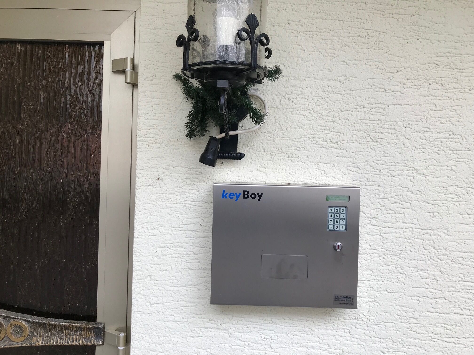 A wall-mounted security panel labeled 'keyBoy' with a keypad and a small display, and a decorative wall-mounted light fixture with a Christmas wreath.