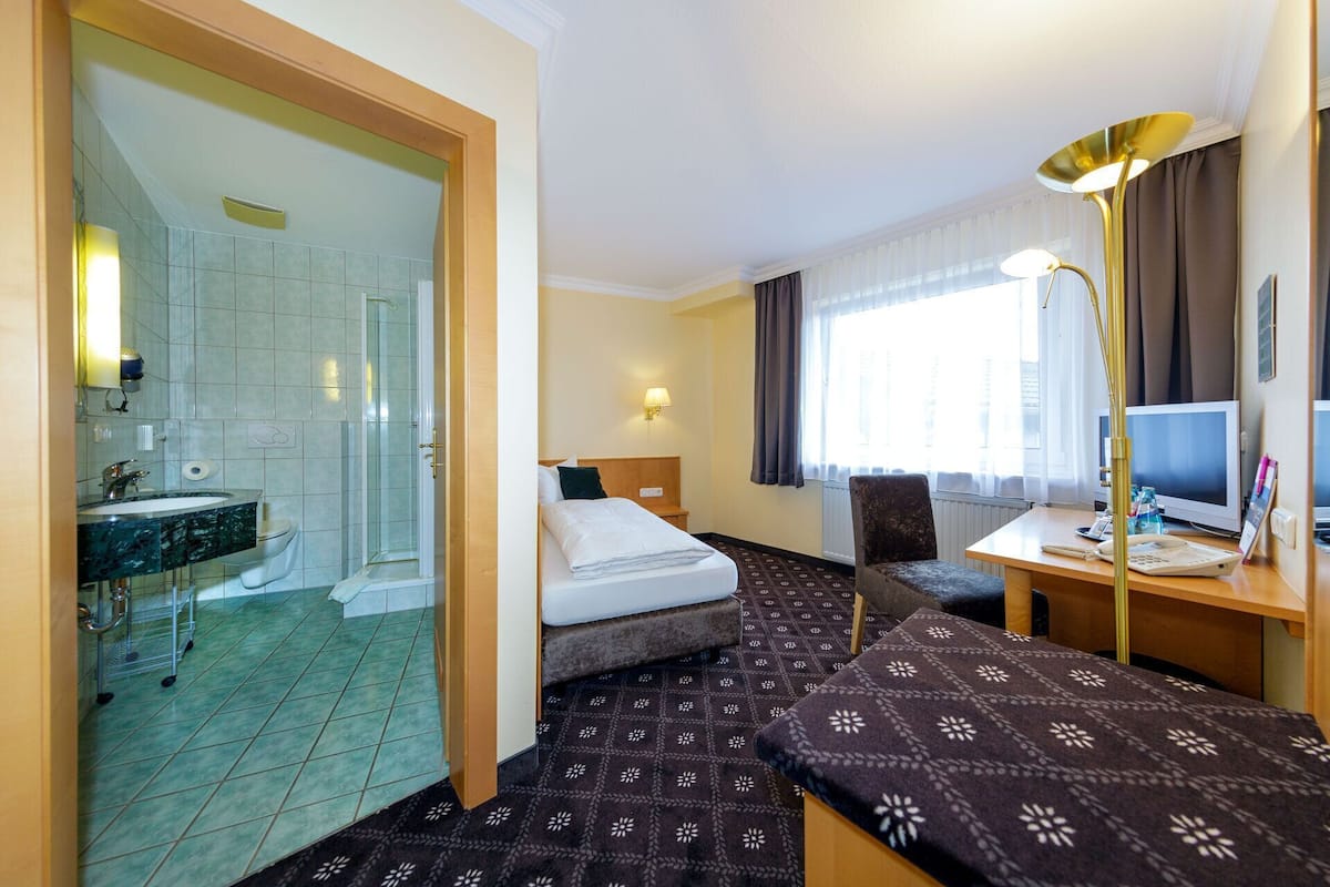 A hotel room with a shower, a bed, a desk with a computer, and a window with curtains.