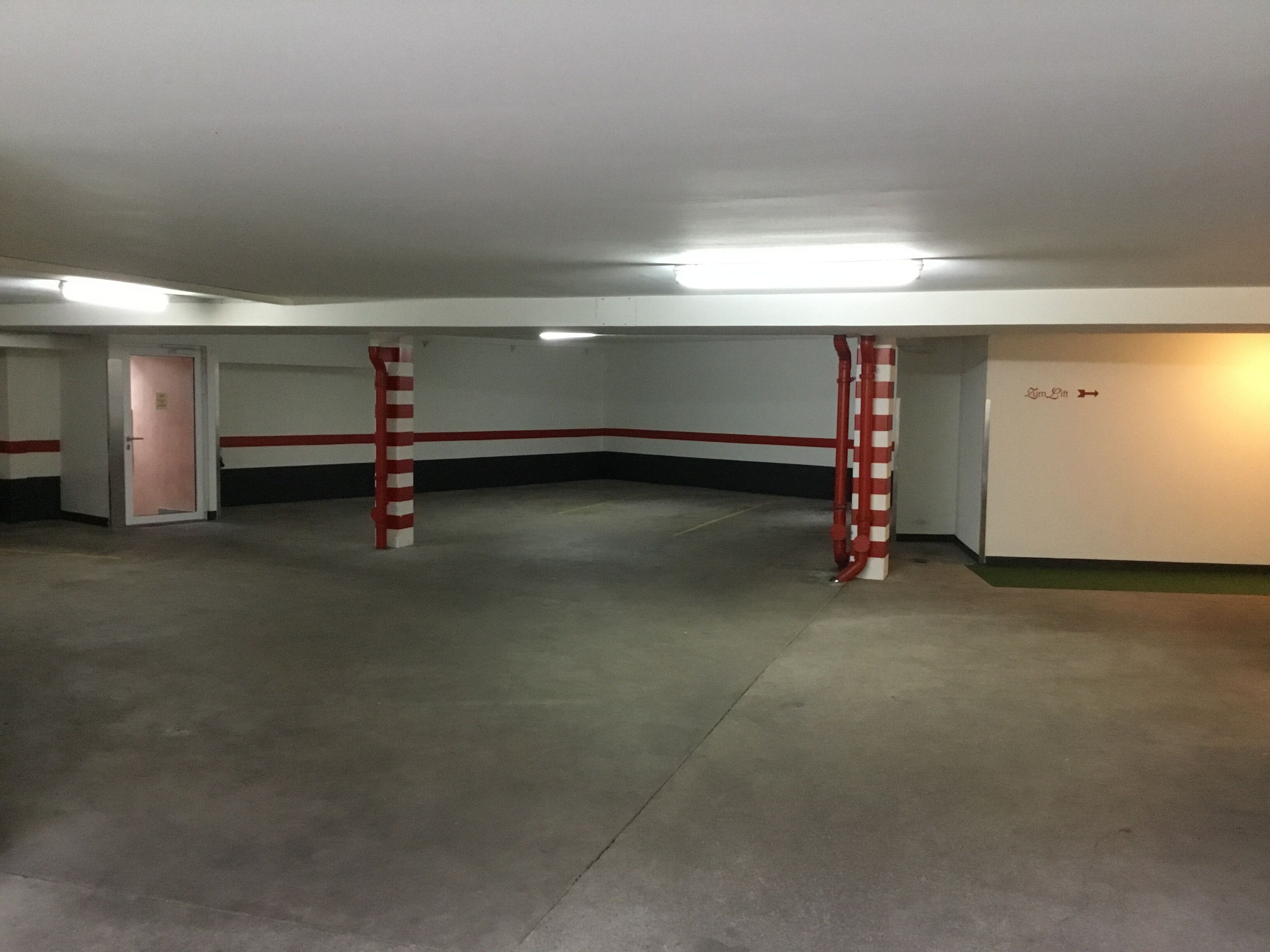 Un estacionamiento con suelo de concreto, barreras rojas y blancas a rayas, y una puerta señalizada con 'Salida'.