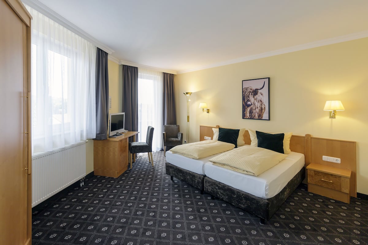 A hotel room with two beds, a desk with a computer, a chair, and a large window with curtains.