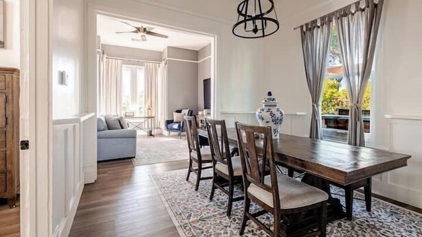 Uma área de refeições com uma mesa e cadeiras de madeira, um tapete estampado e um vaso sobre a mesa.