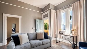 Uma sala de estar moderna com um sofá cinzento, uma mesa pequena e vista para o exterior através de grandes janelas.