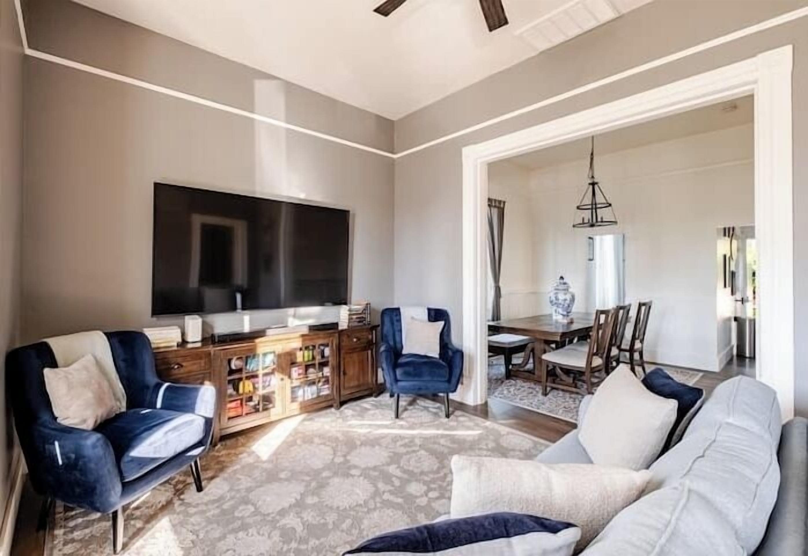 Un salon doté d’un grand téléviseur à écran plat, d’un canapé, de deux fauteuils, d’une table basse et d’un coin repas agrémenté d’un lustre.