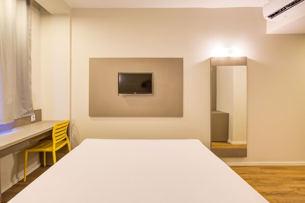 A room with a white desk, a yellow chair, a mounted TV, and a mirror. - Transamerica Fit Rio Verde (Rio Verde)