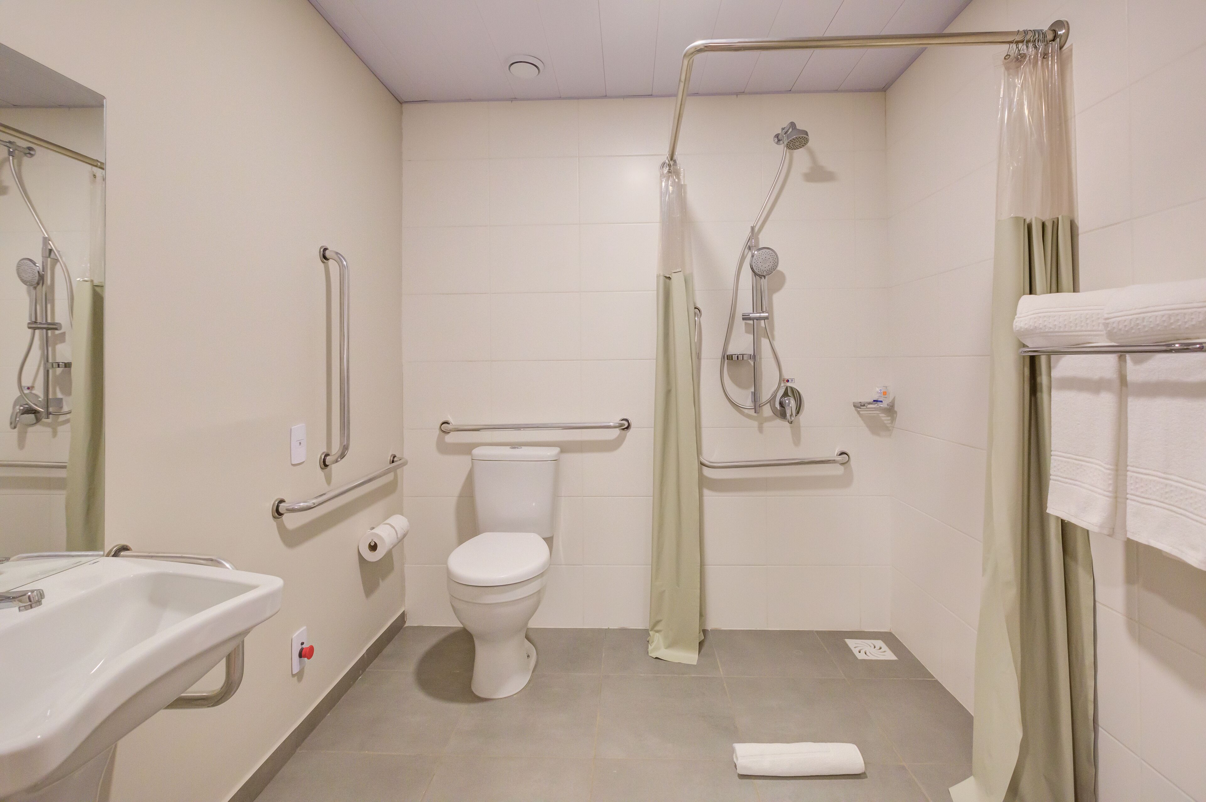 Un baño con inodoro, lavamanos, ducha y barras de apoyo.