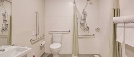 Un baño con inodoro, lavamanos, ducha y barras de apoyo.