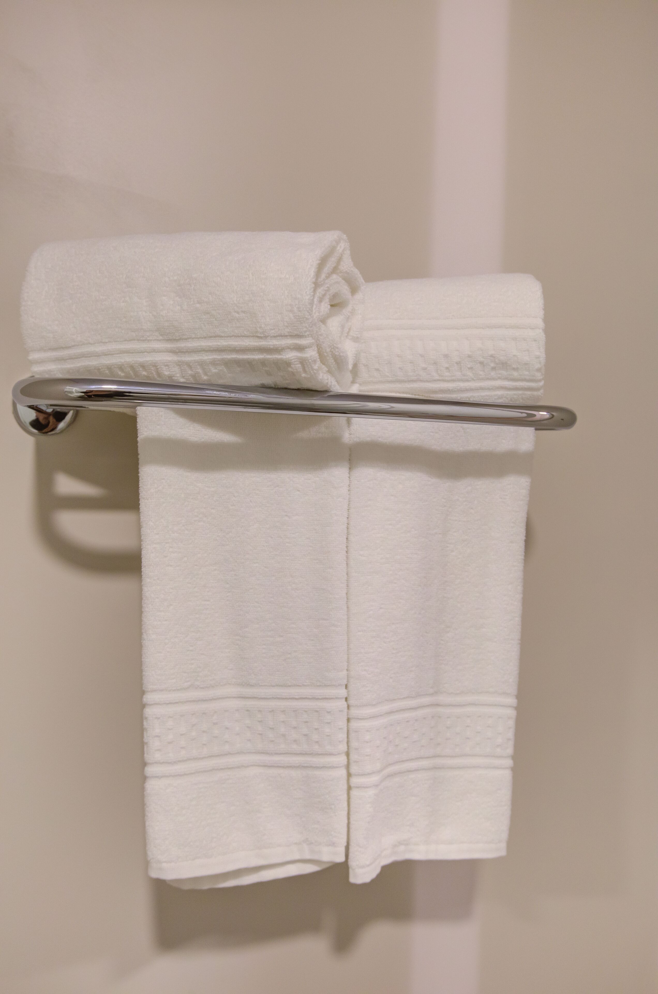 A white towel folded and hanging on a metal towel rack against a plain wall.