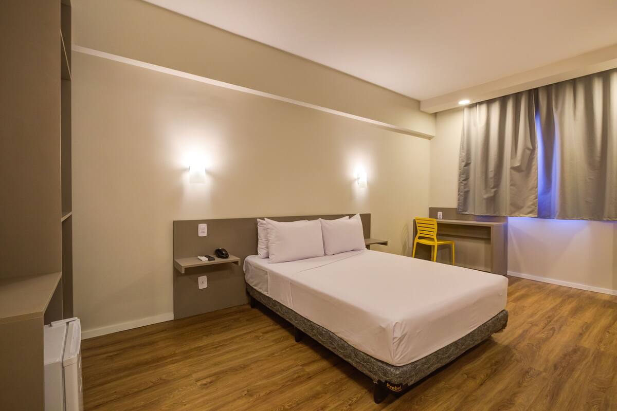 A bedroom with a bed, a desk, a chair, and a nightstand.