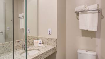 Un baño moderno con cabina de ducha de vidrio, lavamanos de mármol y un inodoro con toallero encima.