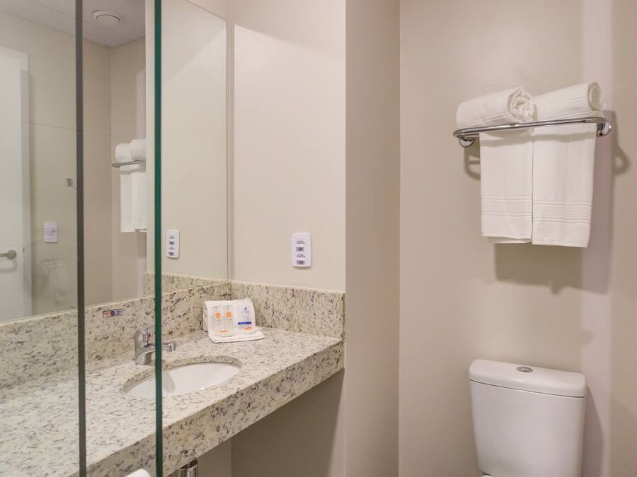 Un baño moderno con cabina de ducha de vidrio, lavamanos de mármol y un inodoro con toallero encima.