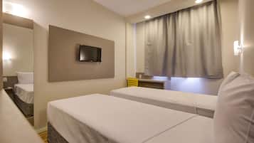 A hotel room with two beds, a TV mounted on the wall, a desk with a chair, and a window with curtains.