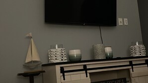 Una sala de estar con un televisor de pantalla plana montado en la pared, una mesa de centro de madera y un mueble con cajones.