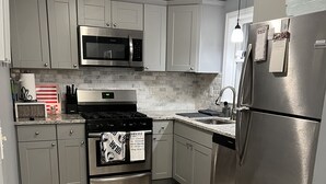 Una cocina moderna con armarios grises, electrodomésticos de acero inoxidable, microondas, estufa y refrigerador.