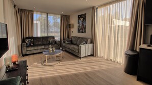 Una sala de estar moderna con dos sofás, una mesa de centro, un televisor y ventanas grandes con cortinas.