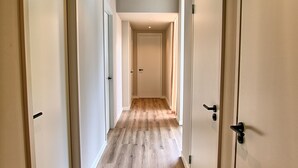 Un pasillo con suelo de madera y paredes blancas, que conduce a una puerta al final.