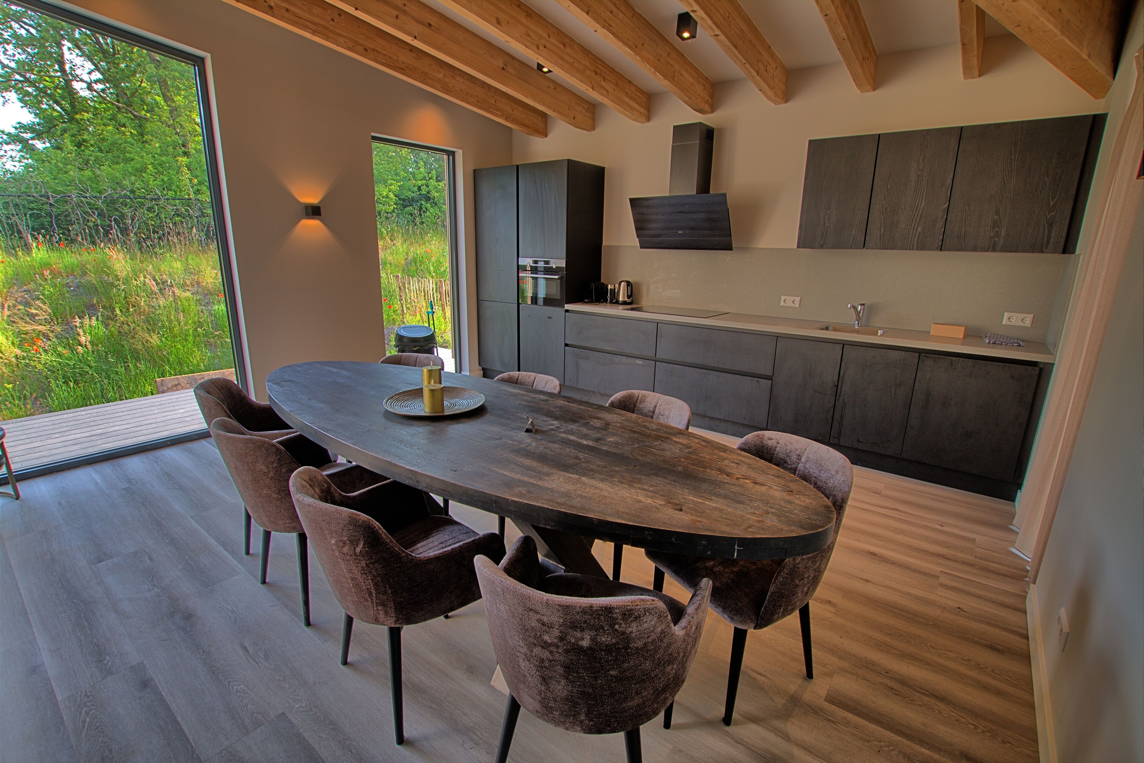 Une cuisine moderne avec des meubles de rangement de couleur sombre, une table à manger en bois et six chaises rembourrées.