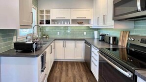 A compact kitchen with white cabinets, a microwave, an oven, and a sink. - Sunsets on the Grand (Lansing)