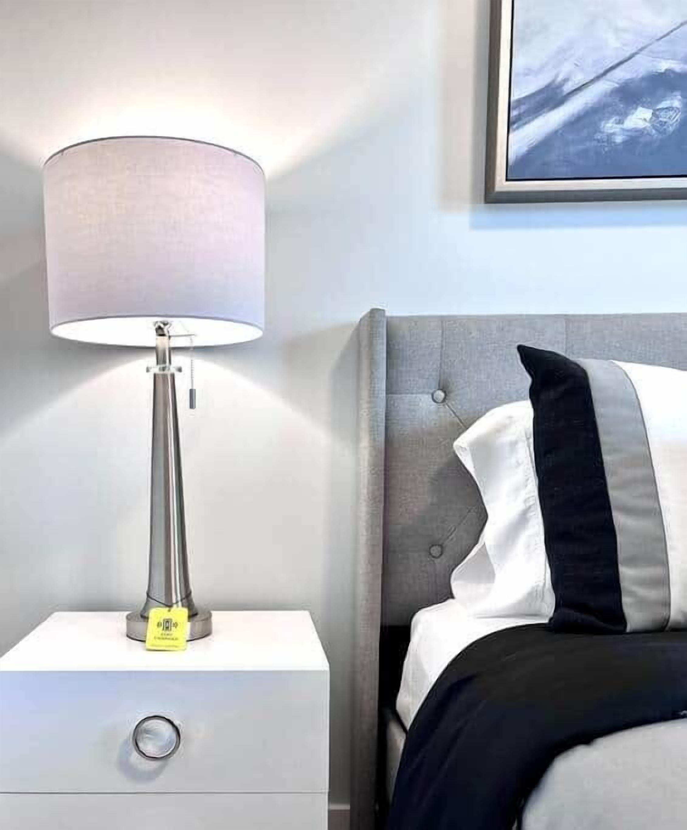 Ein Bett mit grauem Kopfteil, einer Nachttischlampe und einem gerahmten Bild an der Wand.
