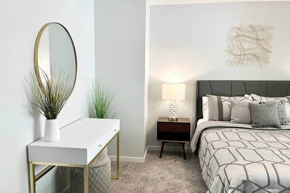 A bedroom with a bed, bedside table, lamp, and a wall-mounted mirror. - Sunsets on the Grand (Lansing)