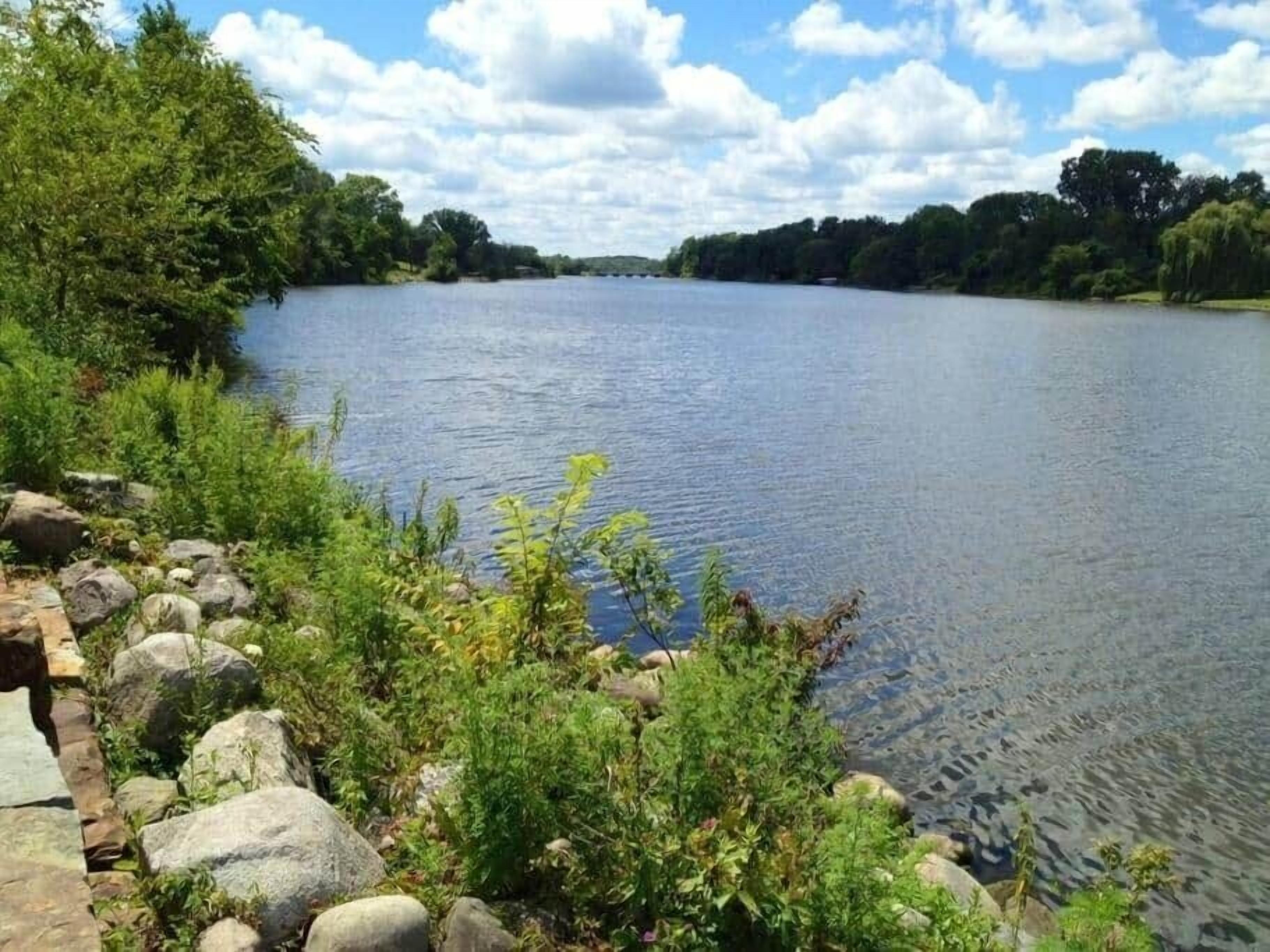 A calm river with a stone pathway and greenery along the banks.