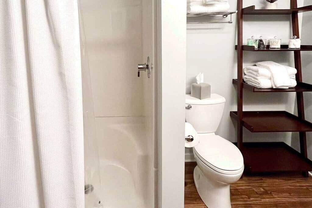 Un baño con inodoro, un estante con toallas y suelo de madera.