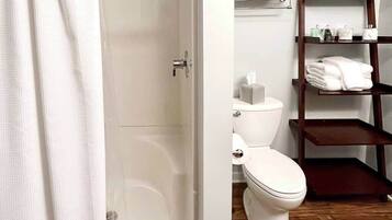 Un baño con inodoro, un estante con toallas y suelo de madera.