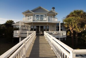 A two-story house with a balcony on the upper floor, a covered porch, and a wooden deck leading to the entrance. - Flexible booking! Oceanfront, 5 bedrooms w/ 4 ensuite, spacious, & beach items. (Fripp Island)