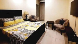Un dormitorio con una cama, una silla, un televisor y una mesita.