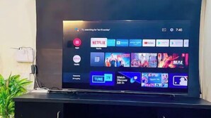 Un téléviseur à écran plat, posé sur un meuble noir, affiche le logo de Netflix, un bouton « TUNE IN » et un bouton « Watch Discover Join In ».