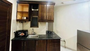 Cocina compacta con armarios de madera oscura, encimera negra, microondas integrado y refrigerador de acero inoxidable.