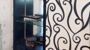 A corner of a room with a decorative black and white patterned wallpaper and a glass display cabinet with various items on shelves. - The Red one bedroom apartment in bahria town (Rawalpindi)