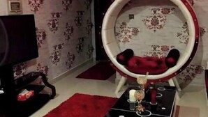 A living room with a round red chair, a flat-screen TV, and a red rug. - The Red one bedroom apartment in bahria town (Rawalpindi)