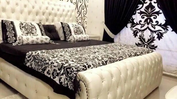 A bedroom with a tufted headboard, a patterned bedspread, and black and white curtains. - The Red one bedroom apartment in bahria town (Rawalpindi)