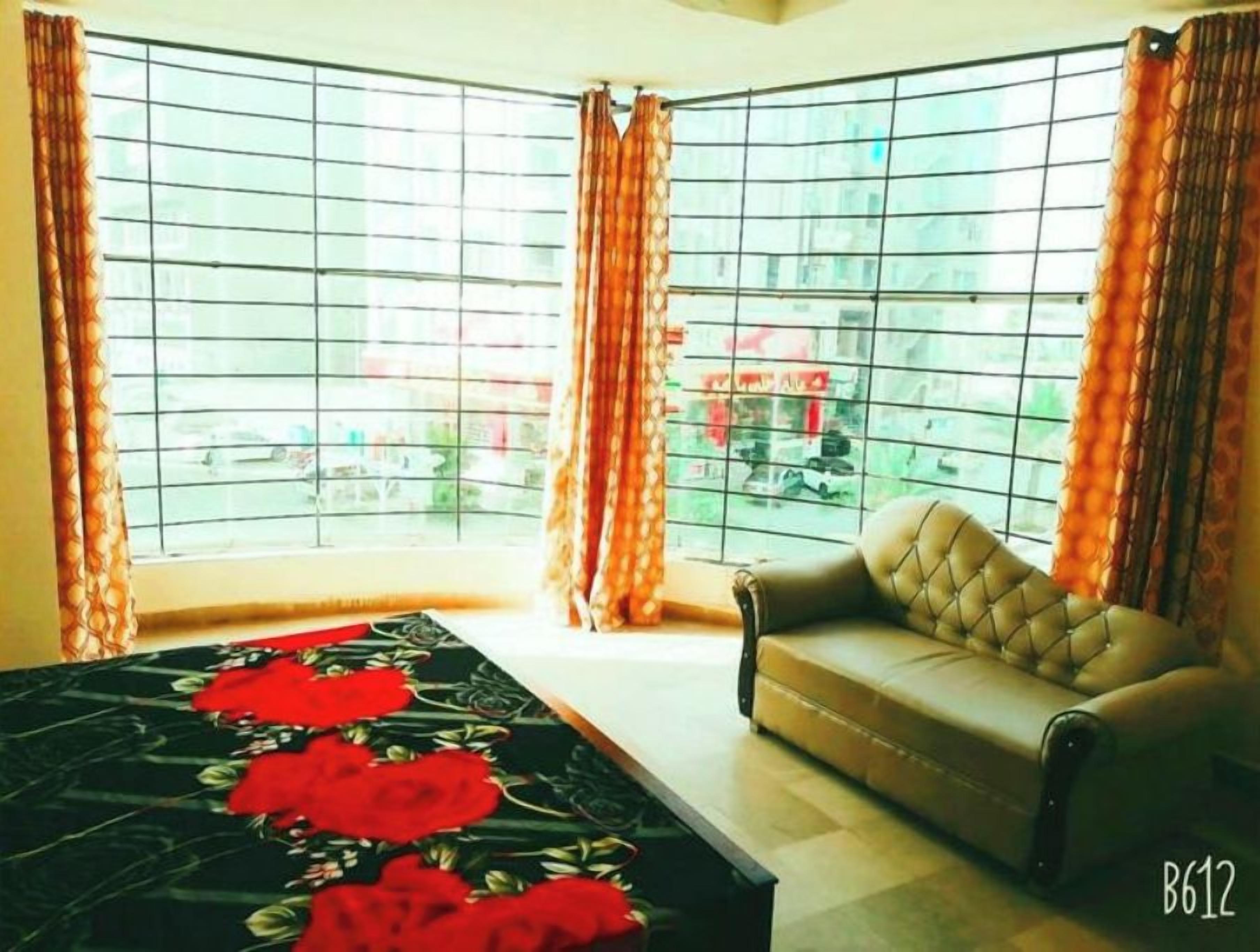 A room with a sofa, a coffee table with a floral table runner, and a view through large windows with curtains.