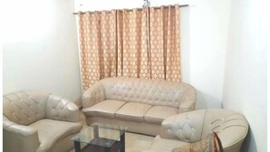 A living room with a beige sofa, two armchairs, and a glass coffee table. - The view apartment in Bahria town. (Rawalpindi)