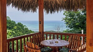 Une terrasse en bois surmontée d’un toit de chaume, avec une table ronde et deux chaises.