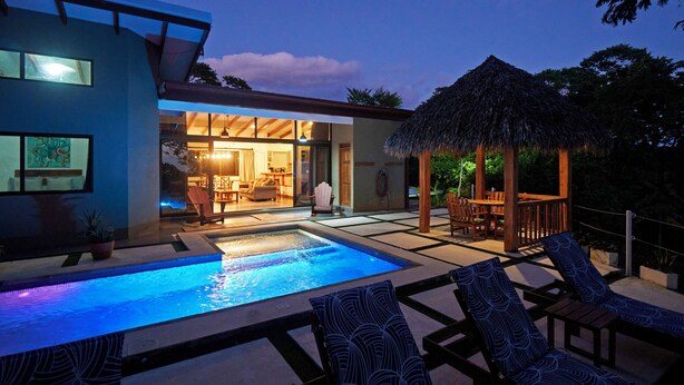 Une maison moderne dotée d’une piscine, de chaises longues et d’un gazebo à toit de chaume.