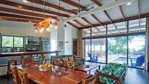 Une cuisine spacieuse avec des poutres en bois, un coin repas avec une table et des chaises en bois, et une grande porte-fenêtre coulissante donnant sur un patio extérieur avec une piscine.