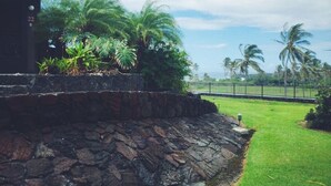 A stone retaining wall with a grassy area and palm trees in the background. - #25 Colony One at Sea Mt. Punalu`u (Pahala)