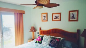 A bedroom with a wooden bed, a ceiling fan, and three framed pictures on the wall. - #25 Colony One at Sea Mt. Punalu`u (Pahala)