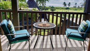 A balcony with two chairs and a table, overlooking a lush landscape with palm trees and a view of the ocean. - #26 Colony One at Sea Mt. Punalu`u (Pahala)