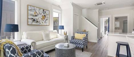 A modern living room with a sofa, patterned armchairs, a coffee table, and a staircase leading to a kitchen area.