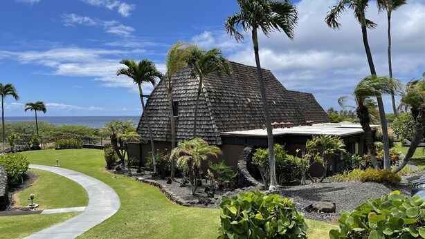 A house with a sloped roof, surrounded by a well-maintained garden with palm trees and shrubs. - #16 2 bed/2 bath Two Story Condo with Stunning Oce (Pahala)