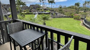 A wooden deck with a table and chairs, overlooking a well-maintained lawn and a pool area with a stone pathway. - #16 2 bed/2 bath Two Story Condo with Stunning Oce (Pahala)