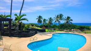 A curved pool with lounge chairs and a view of the ocean. - #16 2 bed/2 bath Two Story Condo with Stunning Oce (Pahala)