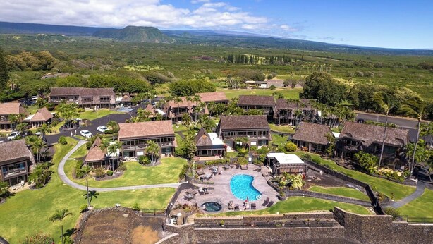 Un resort con varias edificaciones tipo bungalow, una piscina central y un paisaje exuberante con montañas a lo lejos.